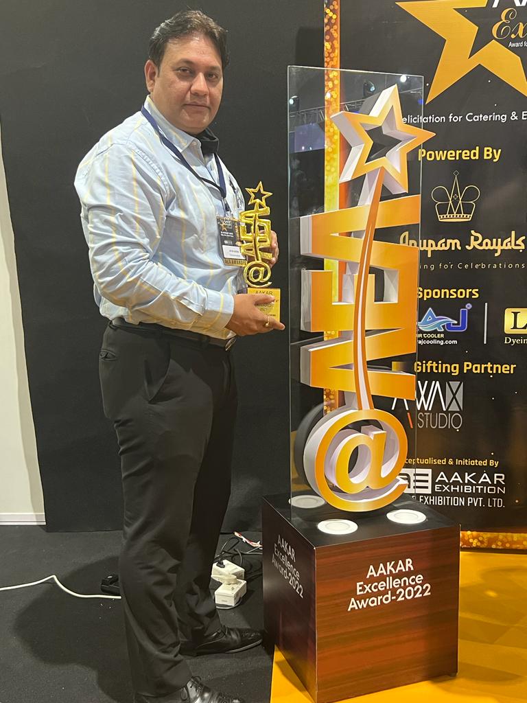 A man holding a trophy beside the large Aakar Excellence Award sculpture