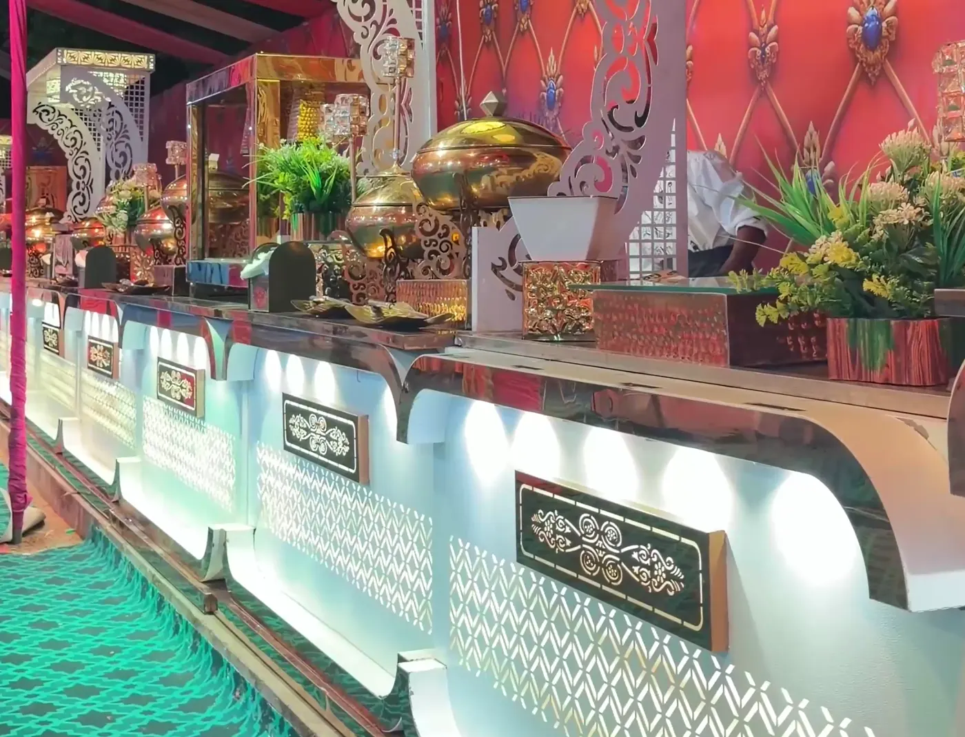 Brass serving dishes and plants along a lit buffet line
