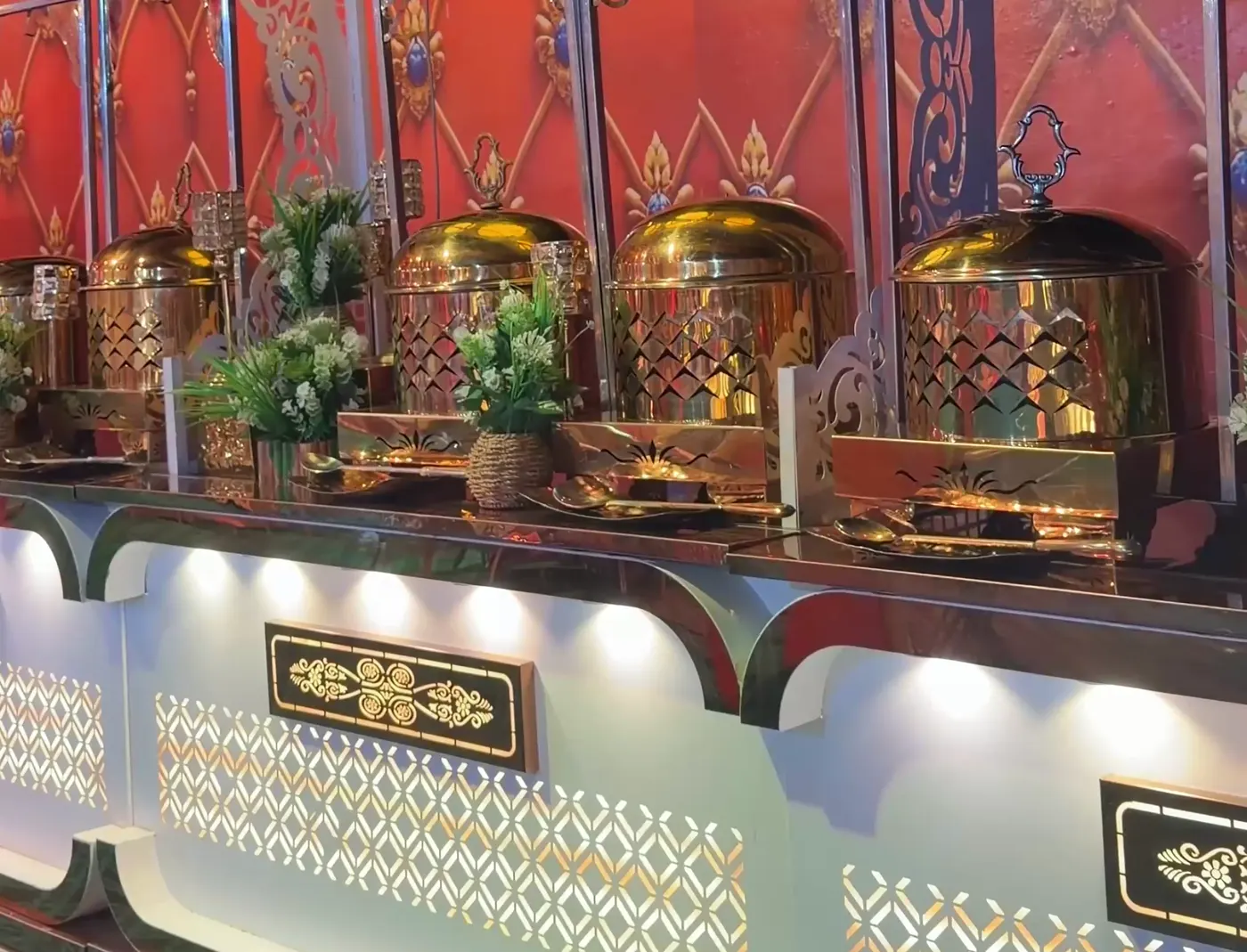 Buffet display with brass dishes against a red patterned backdrop