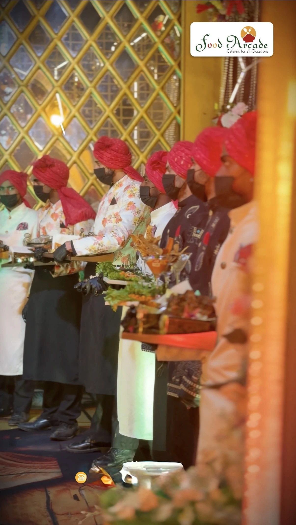 Hospitality team in turbans and festive jackets holding trays of starters and garnished food