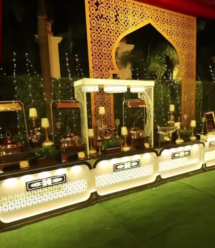 Lit buffet counters on a lawn beneath a carved gateway at night
